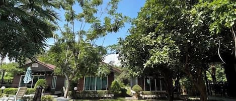 Um pátio com área de refeições, espaço coberto para sentar e uma grande árvore que oferece sombra.