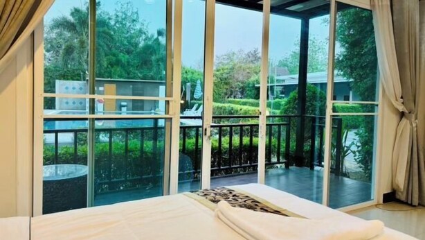 Une chambre dotée d’une grande porte-fenêtre coulissante donnant sur un balcon avec vue sur la verdure et une piscine.