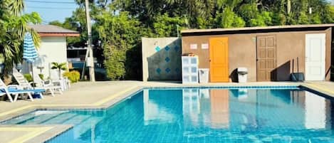 A swimming pool with lounge chairs and a small building with a door and windows.