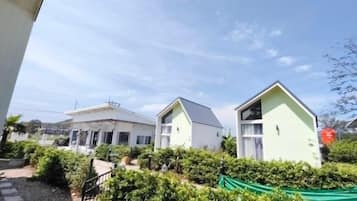 A residential area with two houses, one with a sloped roof and another with a flat roof, surrounded by greenery and a clear sky.