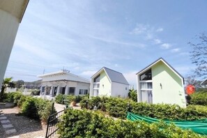 A residential area with two houses, one with a sloped roof and another with a flat roof, surrounded by greenery and a clear sky. - Luciano Homestay (Thepha)