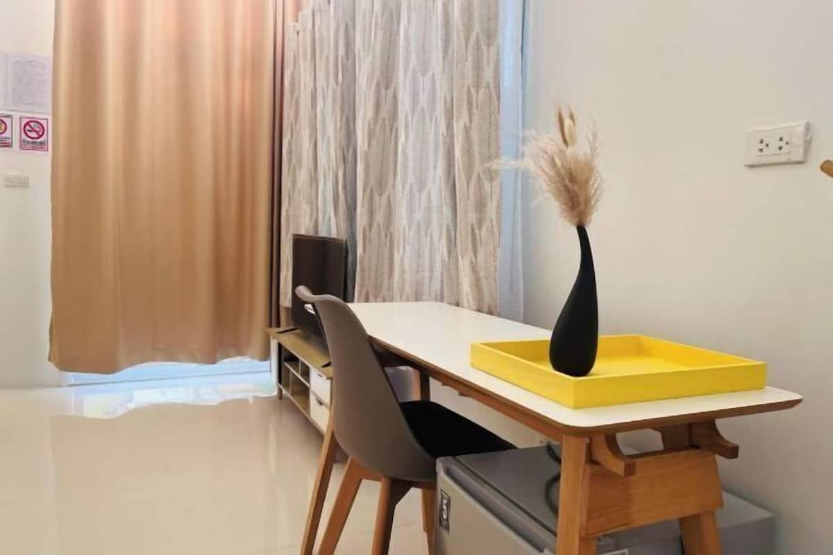 A small dining area with a white table, a yellow tray, a black vase with dried plants, and a grey chair.