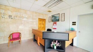 Zona de recepción de un hotel con un mostrador de madera, una silla rosa y un letrero en la pared.
