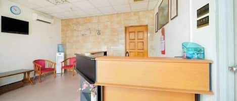 Un área de recepción con un escritorio de madera, una silla, un televisor y un reloj de pared.