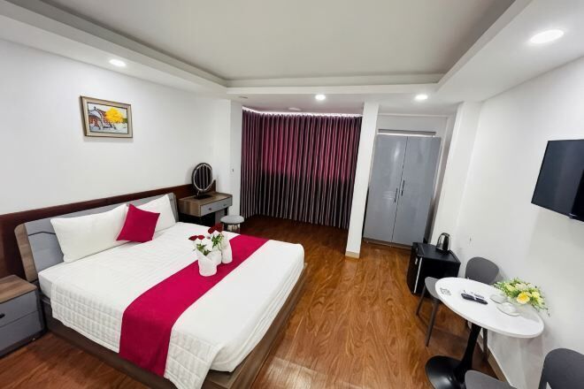 A hotel room with a bed, bedside table, TV, and a small dining area.