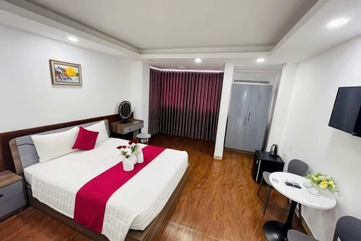 A hotel room with a bed, bedside table, TV, and a small dining area.
