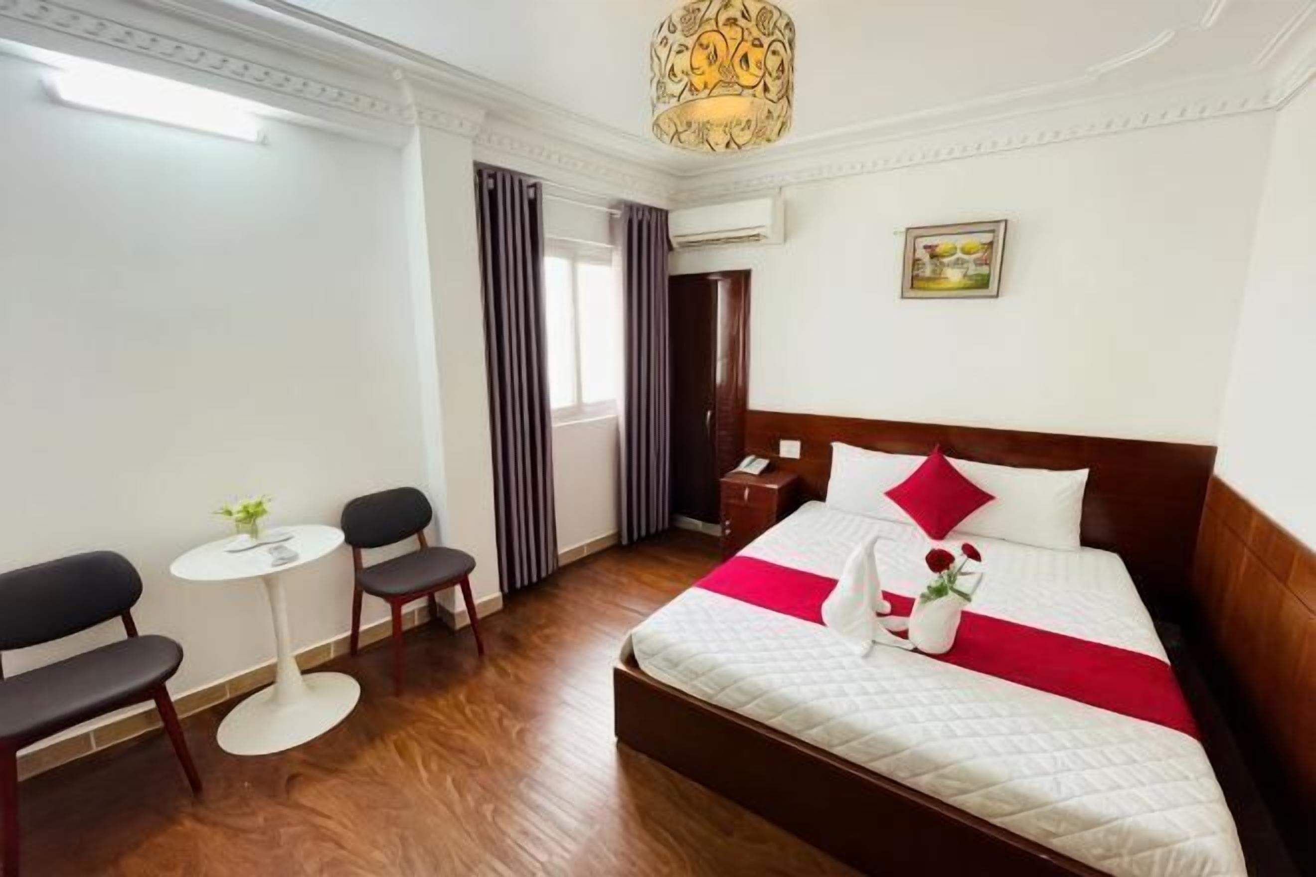 A hotel room with a bed, a small table, two chairs, a window with curtains, and a painting on the wall.