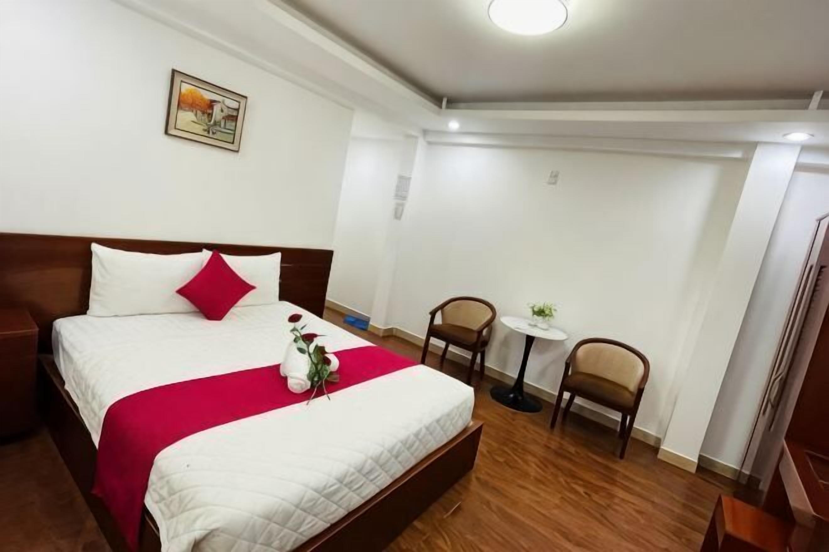 A hotel room with a bed, a small table, two chairs, and a single wall-mounted light.