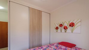 Un dormitorio con una cama, un cojín rojo, una puerta de madera y un cuadro de flores rojas en la pared.