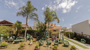 Un jardín con varias esculturas y plantas, un sendero y edificios al fondo.