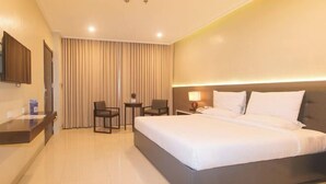 A hotel room with a large bed, a desk, a chair, a small table, and a TV on the wall. - Iloilo Gateway Hotel and Suites by RedDoorz (Pavia)