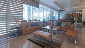 A spacious living area with a large sofa set, a coffee table, and a dining table. There are large windows providing natural light and a view of the outdoors. - Iloilo Gateway Hotel and Suites by RedDoorz (Pavia)