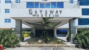 A modern building with a sign reading "Gateway Hotel." It features a covered entrance with a palm tree in the center, surrounded by greenery. - Iloilo Gateway Hotel and Suites by RedDoorz (Pavia)