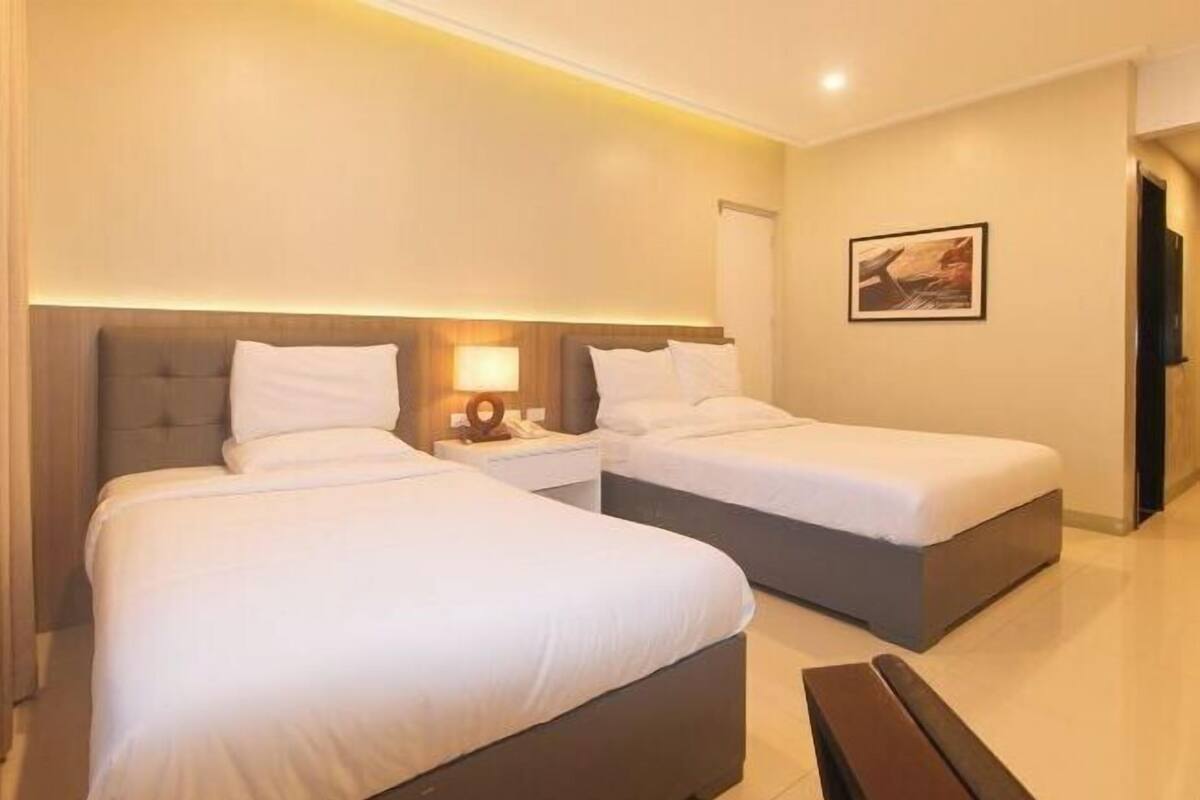 Een hotelkamer met twee bedden, een nachtkastje met een lamp, en een schilderij aan de muur.