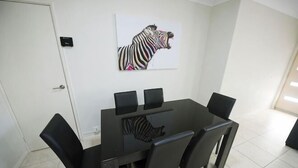 A dining area with a black table and chairs, a zebra artwork on the wall, and a door to the left. - Unit Close to Airport, Hospital, Shops & Transport (Midland)