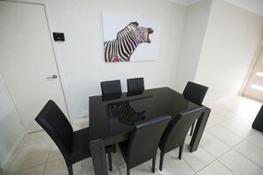A dining area with a black table and chairs, a zebra artwork on the wall, and a door to the left. - Unit Close to Airport, Hospital, Shops & Transport (Midland)