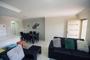 Una sala de estar con un sofá negro, una mesa de comedor con sillas, una zona de cocina y una puerta con ventanal.
