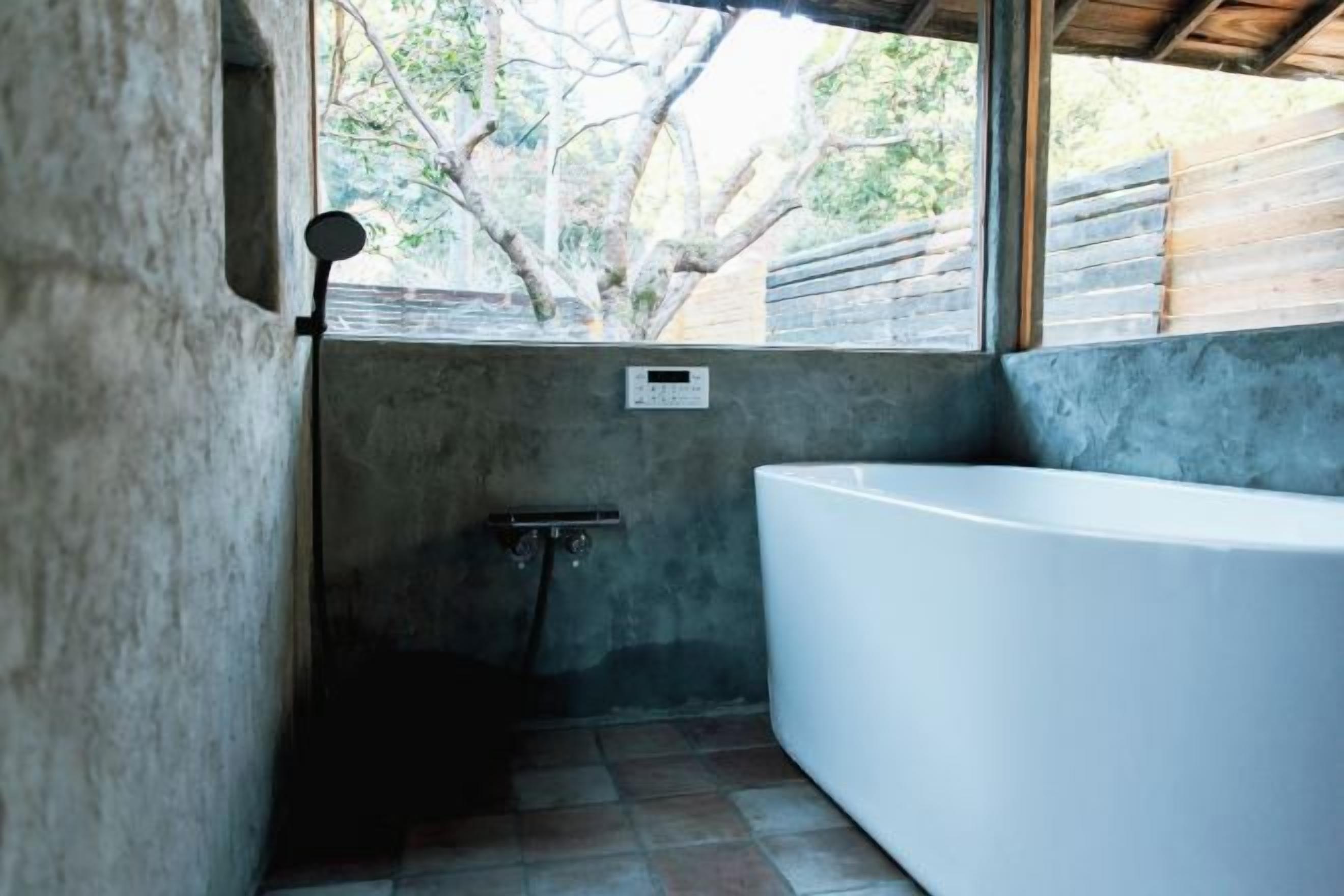 A bathroom with a large bathtub, a window with a view of trees, and a shower area.