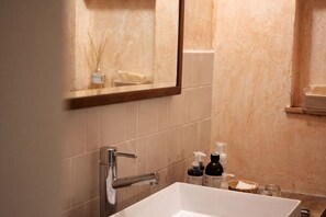 Un baño con un lavamanos blanco, un espejo y artículos de aseo en la encimera.