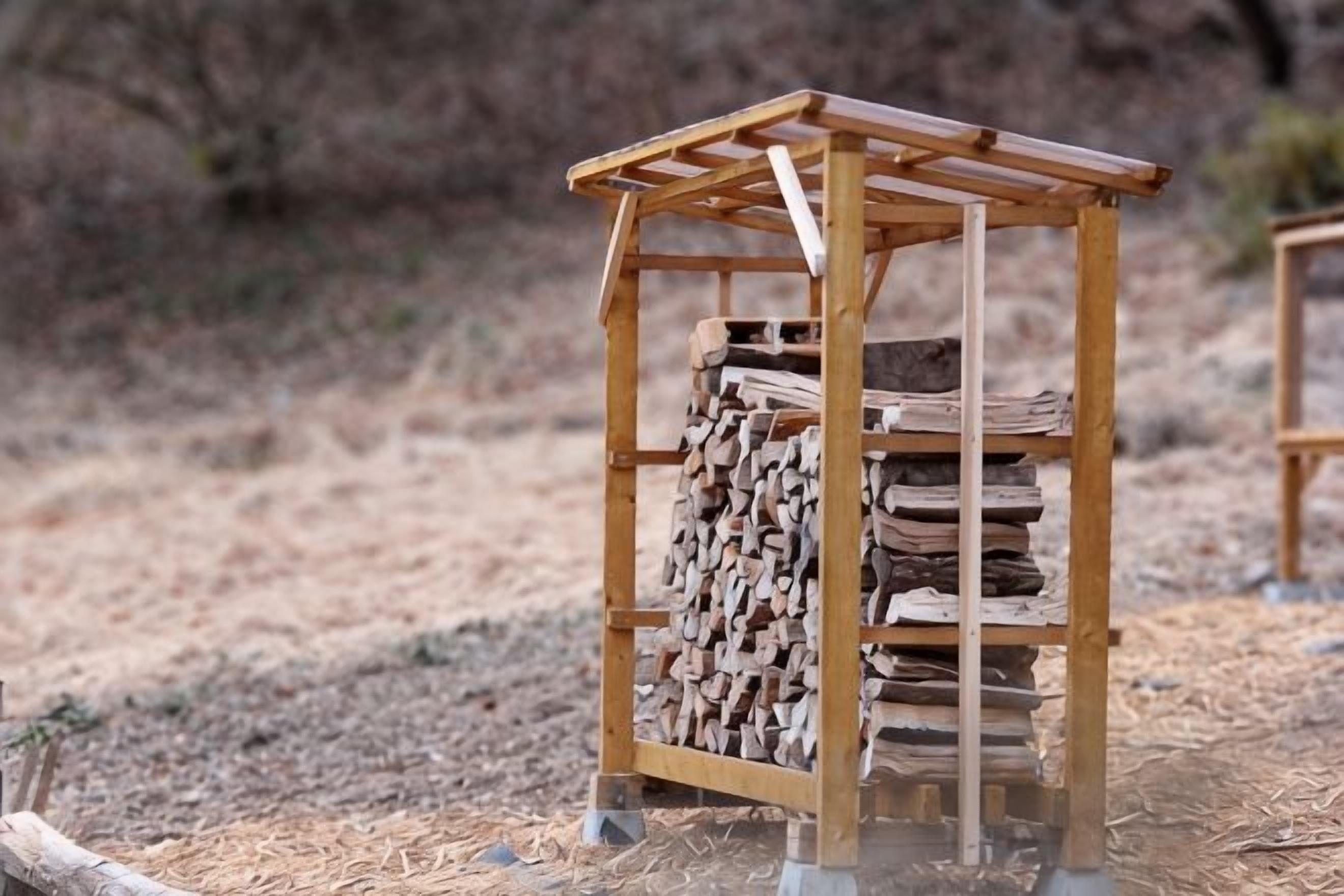 A wooden structure with a roof, possibly a shed or storage unit, with stacked firewood inside.
