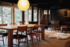 A cozy interior with a dining table, chairs, a sofa, and a large window offering a view of trees.