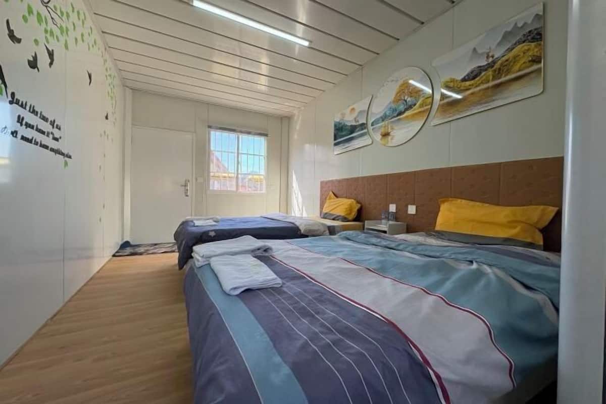 Une chambre d’hôtel avec deux lits, un plancher en bois, une fenêtre et des œuvres d’art murales.