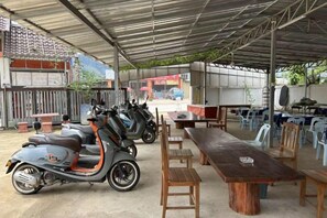 A covered outdoor area with a dining table, chairs, and two scooters. - golden sunrise guesthouse (Vang Vieng)