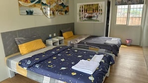 A hotel room with two beds, each with a different patterned bedspread. There are wall art pieces above the beds, a window with a view of the outdoors, and a small trash bin near the window. - golden sunrise guesthouse (Vang Vieng)