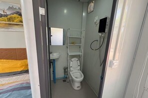 A small bathroom with a toilet, a sink, a mirror, and a shelf. - golden sunrise guesthouse (Vang Vieng)