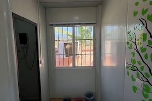 Una habitación pequeña con ventana, puerta y pared decorada con un dibujo de un árbol.
