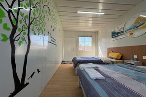 A hotel room with two beds, a wooden floor, a window, and a wall with a tree mural. - golden sunrise guesthouse (Vang Vieng)