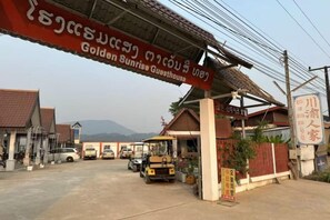 A guesthouse with a signboard, a covered parking area, and a view of mountains in the background.