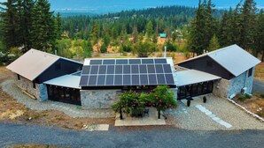Een modern gebouw met een schuin dak en zonnepanelen, omringd door een bos en bergen op de achtergrond.