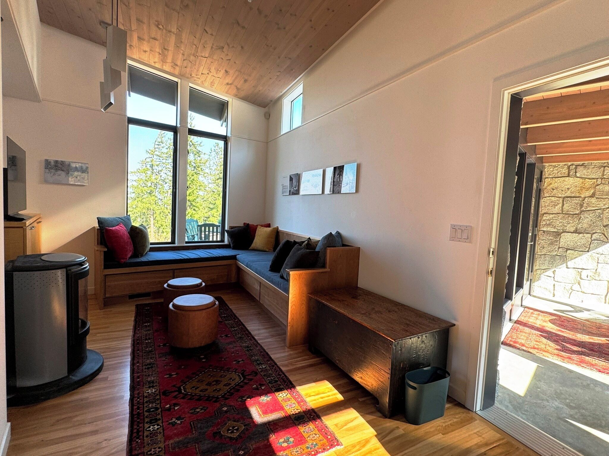 A cozy living room with a wooden bench, a sofa with cushions, a rug, and large windows.