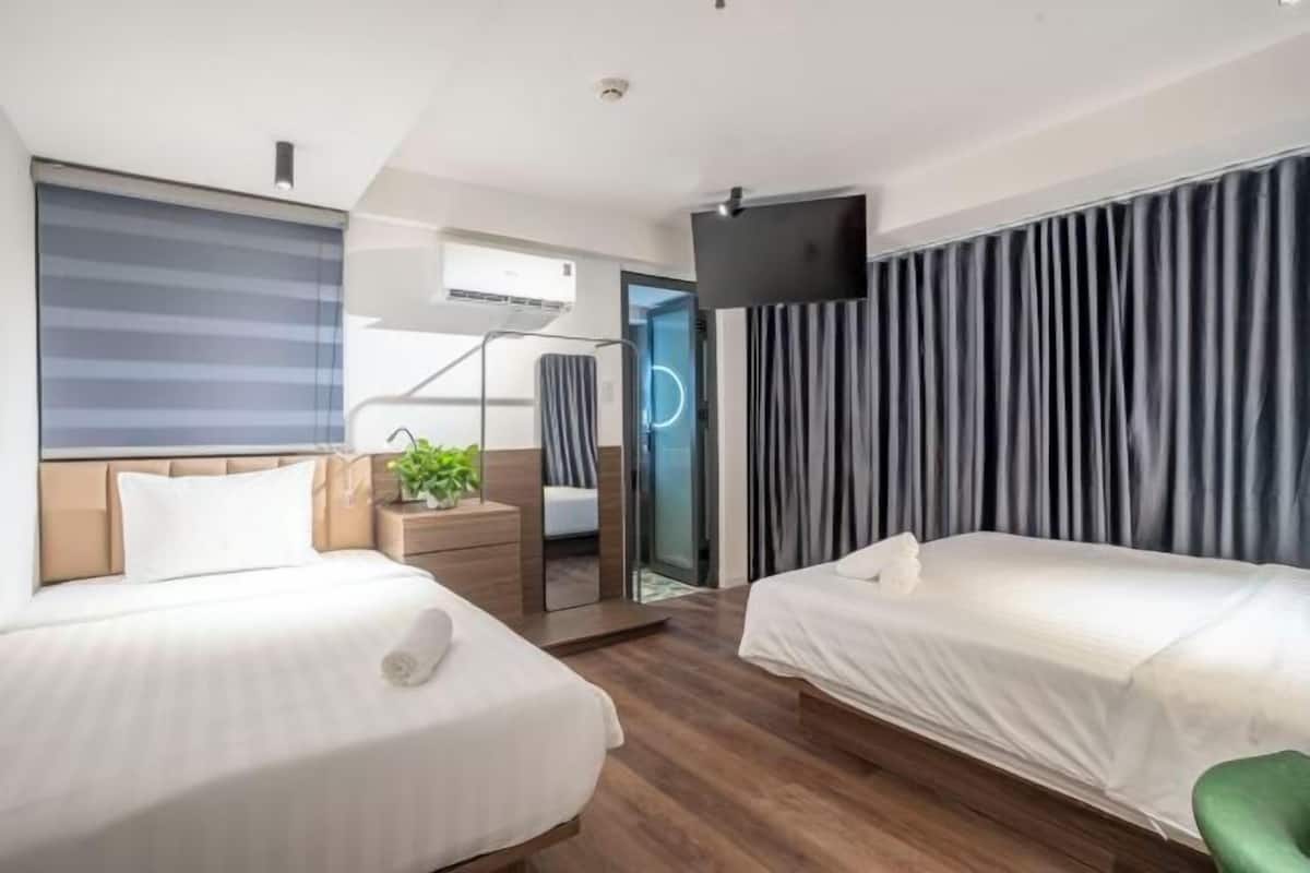 Ein Hotelzimmer mit zwei Betten, einem Fernseher, einem Spiegel und einer Schiebetür zu einem Badezimmer.