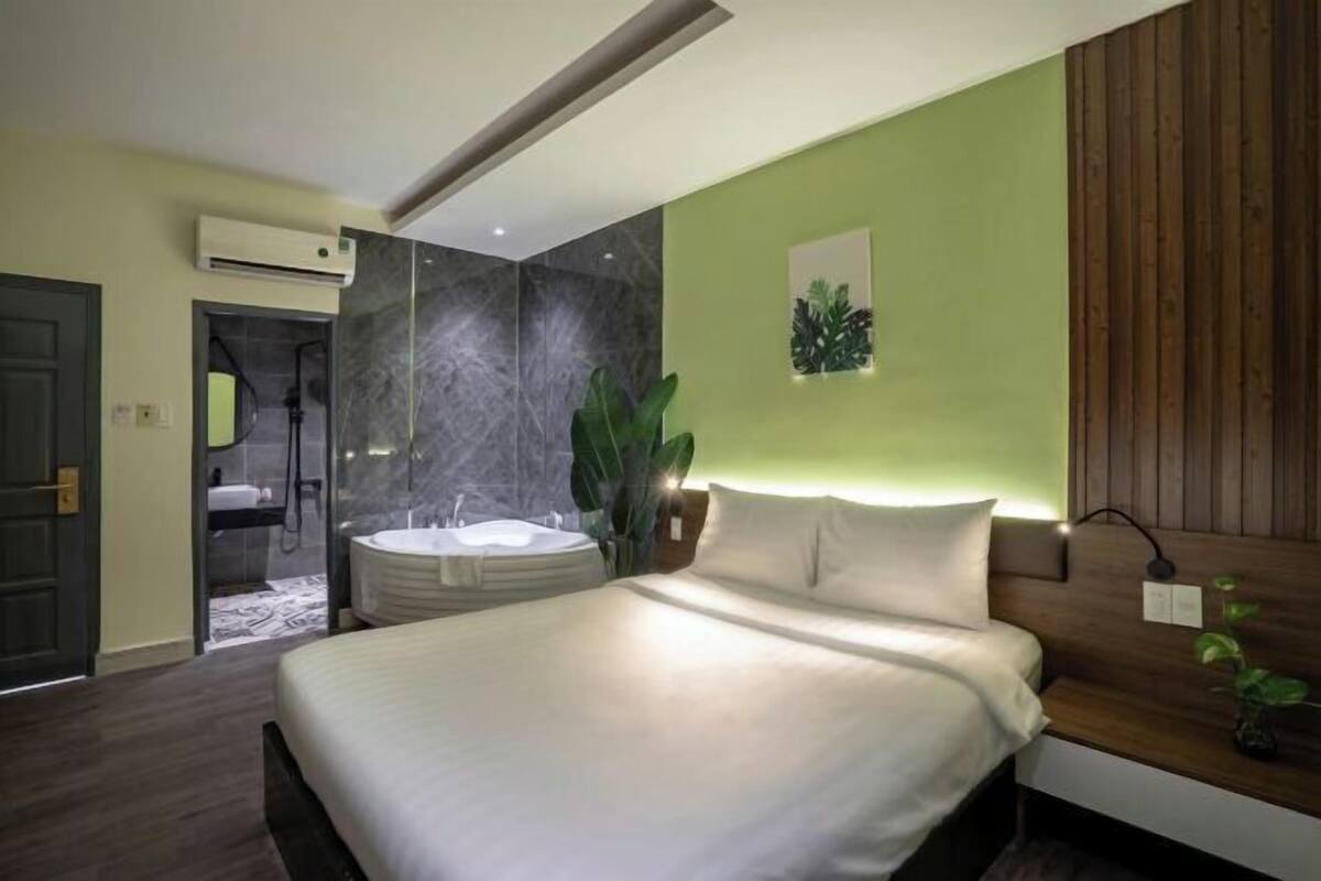 Ein modernes Hotelzimmer mit einem großen Bett, einem an der Wand montierten Fernseher, einem kleinen Nachttisch und einem Duschbereich.