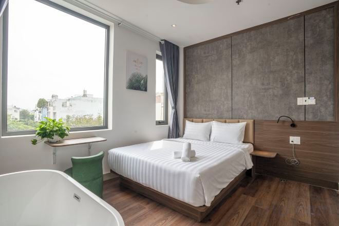 A modern bedroom with a large bed, a window, a green chair, and a wooden wall.