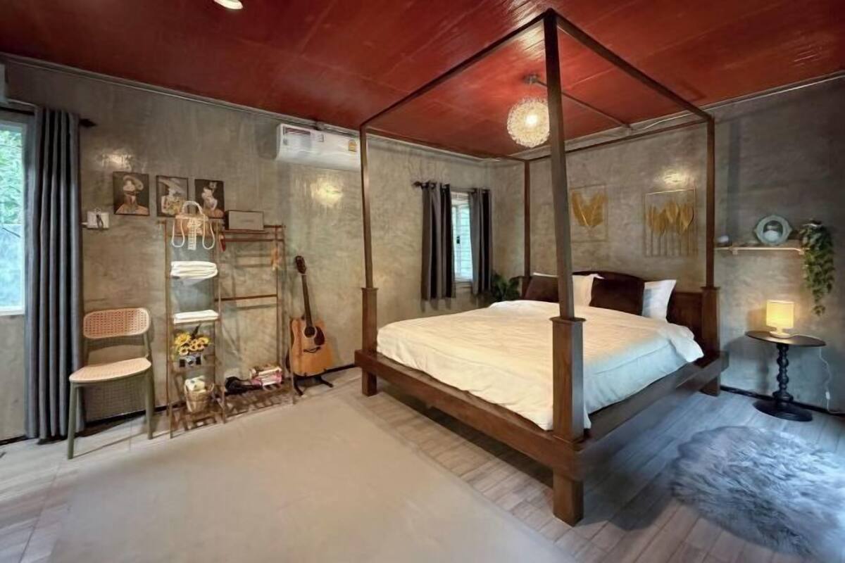 Una cama con dosel de madera, una guitarra y una silla con asiento de fibras tejidas.