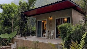 A small, single-story building with a red roof and a covered patio area. There are two white chairs and a table on the patio. - Vrapat (Chiang Dao)