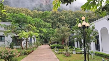 A pathway leading to a building with a traditional architectural style, surrounded by lush greenery and a clear sky.