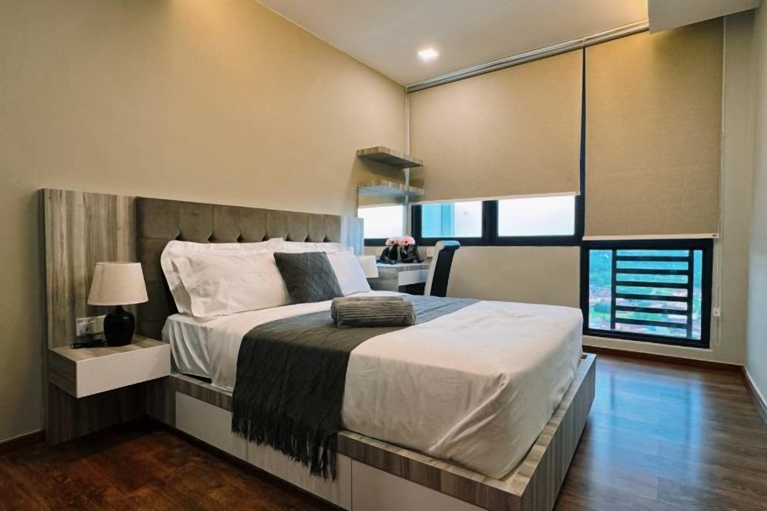 A modern bedroom with a large bed, a nightstand, a lamp, and a window with blinds.