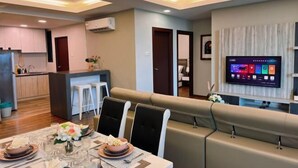 Een moderne woonkamer met een bank, een eethoek met een tafel gedekt voor vier personen, en een keuken met een bar.