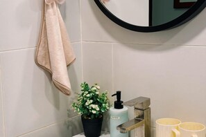 A bathroom with a towel hanging on the wall, a potted plant, a soap dispenser, and two cups on a shelf. - Kuching Vivacity Jazz Suite l 2BR Suite (Kuching)