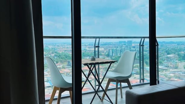 Een balkon met een tafel en twee stoelen, met uitzicht op een stadslandschap met gebouwen en groen.