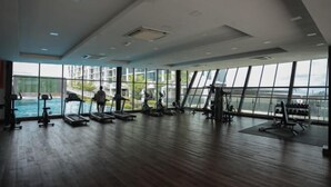 Een ruime fitnessruimte met diverse trainingsapparaten, grote ramen en uitzicht op een waterpartij.