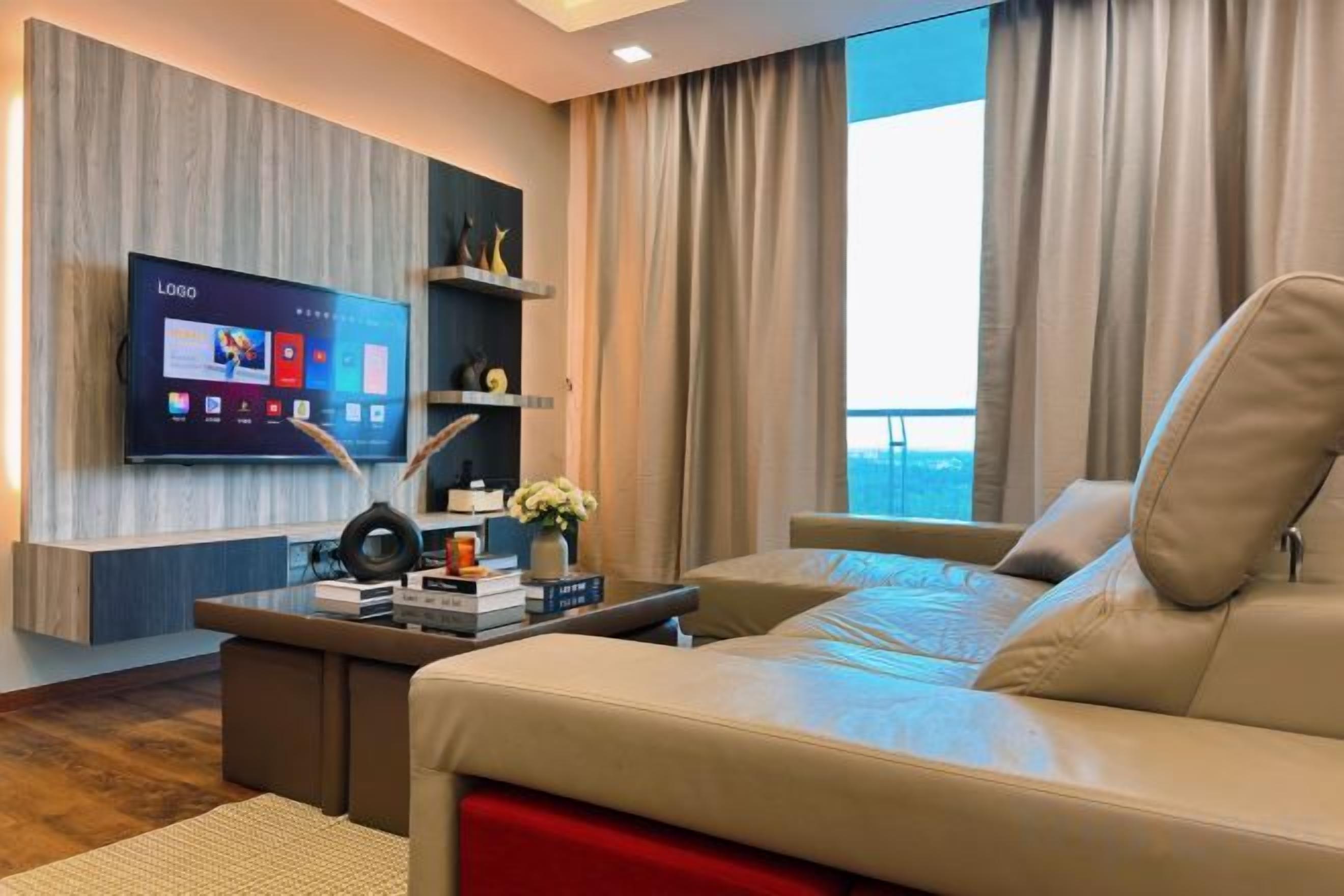 A modern hotel room with a large flat-screen TV, a sofa, a coffee table, and a view of the outdoors.