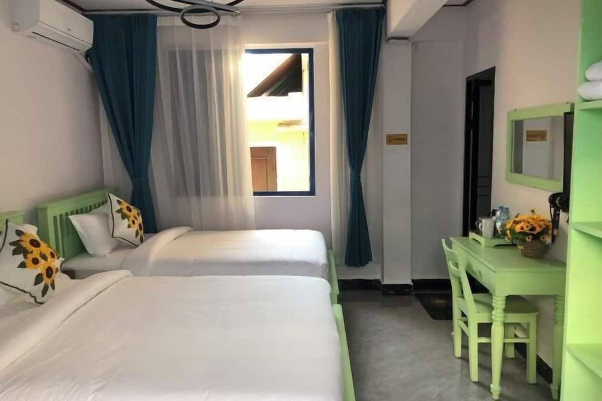 Une chambre d’hôtel avec deux lits, un bureau, une chaise et une fenêtre avec des rideaux.