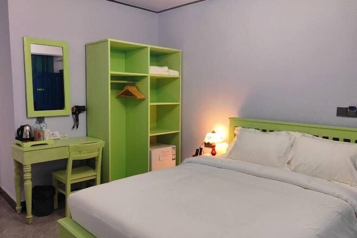 Une pièce comprenant un lit, une armoire verte, un bureau et un miroir.