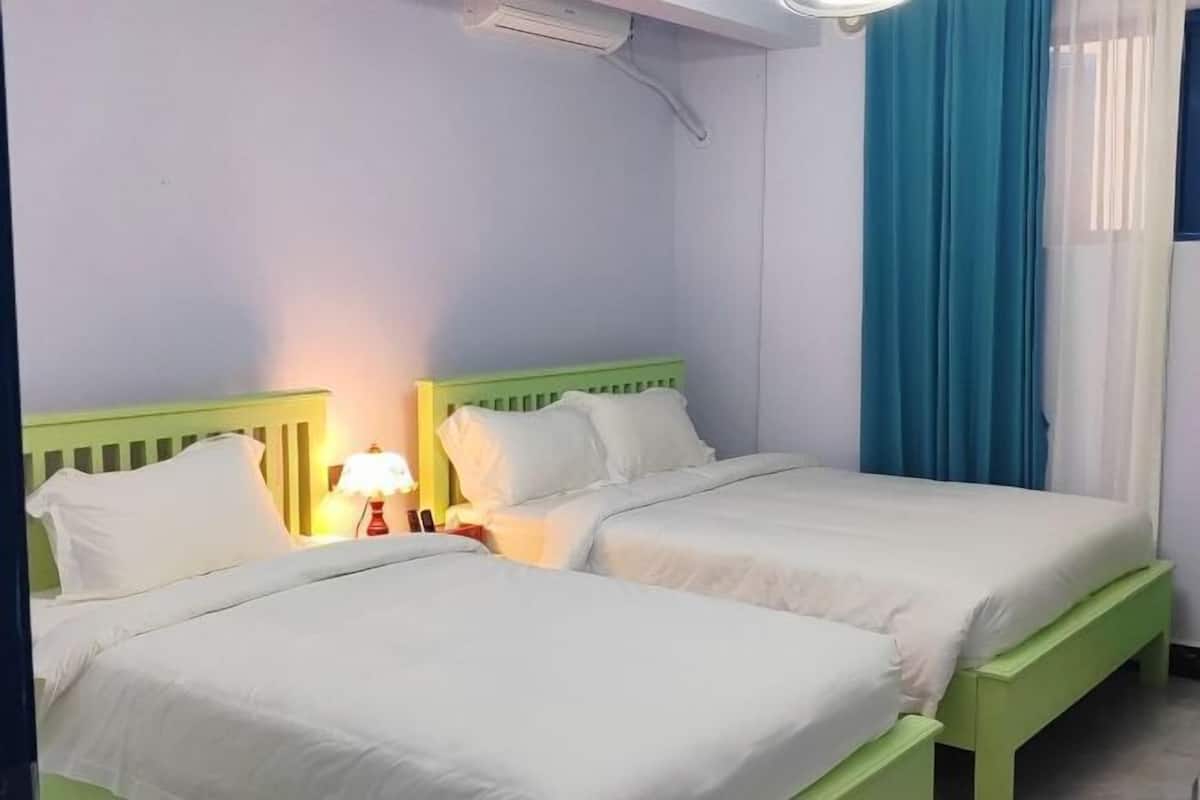 Une chambre double avec deux lits, une table de chevet avec une lampe et une fenêtre avec des rideaux bleus.