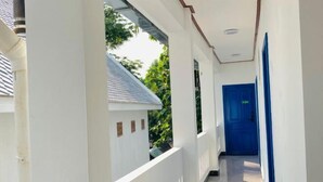 A corridor with white walls, a blue door, and a view of a house outside. - Vip Kingson Guest House (Luang Prabang)